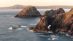 Rocky coastal cliffs with a natural arch opening to the sea, bathed in golden hour light.