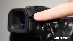 Close-up of a finger touching the eyepiece of a black mirrorless camera with visible control buttons and indicators.