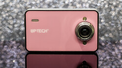 Pink compact digital camera with chrome lens ring against sparkly gray background.