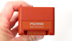 Red PS099E 99Wh V-mount battery held in hand, showing terminal connectors on front panel.