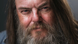 Bearded man with long hair and intense expression in close-up portrait.