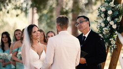 Bride and groom exchange vows at outdoor wedding ceremony with officiant and guests watching.