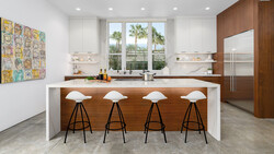 Modern kitchen interior with wood and white island featuring four bar stools, stainless steel appliances, and palm tree views through large windows.