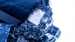 Digital watch covered in snow and ice against a blue winter background.