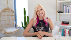Woman with platinum blonde hair and pink underlights smiling at camera in bright studio setting.