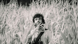 Man in cornfield holding corn stalks, smoking cigarette in black and white photograph.