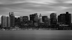 Monochrome cityscape with illuminated skyscrapers reflected in still water at dusk.