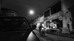 Nighttime street scene with parked truck, pedestrians, and storefronts illuminated by streetlight.