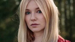 Portrait of a woman with platinum blonde hair and blue eyes against a blurred forest background.