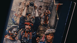 Photographer holding camera overhead while street performers pose below in urban setting.