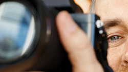 Male photographer looking through a telephoto lens with shallow depth of field focus on his eye.