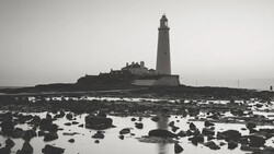 Lighthouse on rocky tidal flats under overcast sky in black and white.