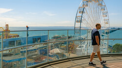 Runner jogging on a seaside boardwalk with a Ferris wheel and amusement park visible in the background.