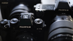 Fujifilm X-T5 camera with attached lens and additional camera gear in background.