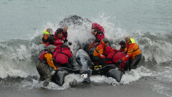 Rescue team in inflatable boat navigating through ocean waves during active water conditions.