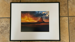 Framed photograph of a dramatic sunset over a desert rock formation with golden and orange sky.