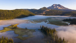 Snow-capped volcanic peak rising above forested valleys with layered lakes and morning mist.