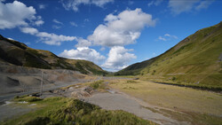 Alpine valley with braided river, grassy slopes, and dramatic sky with white clouds.