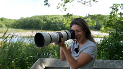Photographer with telephoto lens overlooking a wetland landscape with reeds and trees.