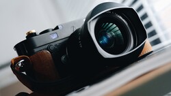 Rangefinder camera with brown leather strap and wide-angle lens, held in hand against blurred background.