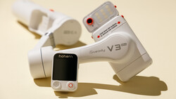 Three white handheld video stabilizers and a smartphone mounted on a neutral beige surface with soft shadows.