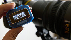 A blue GPS watch displaying navigation data held in front of a camera with telephoto lens.
