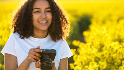 Young photographer holding a mirrorless camera in a bright yellow flower field during golden hour.