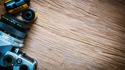 Vintage camera with interchangeable lenses and film rolls arranged on wooden surface.