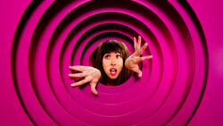 Person with surprised expression emerging from center of concentric black circles on magenta background.