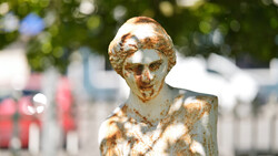Weathered golden bust sculpture with shallow depth of field and blurred background.