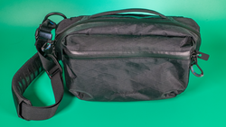 Black shoulder bag with multiple zippered compartments and an adjustable strap against a teal background.