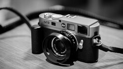 Leica M9 rangefinder camera with black leather strap on wooden surface.