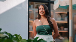Woman in green halter top and white skirt smiling outdoors in natural sunlight.