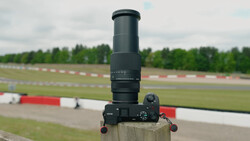 Sony mirrorless camera with telephoto lens mounted on wooden post overlooking racing circuit.