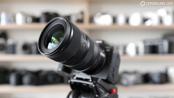 Black zoom lens mounted on camera body positioned on tripod against blurred equipment shelves.
