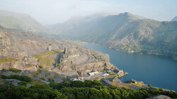 Medieval fortress on a rocky peninsula overlooking a deep blue alpine lake surrounded by mountains.