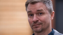 Man with gray hair and facial hair looking at camera with a skeptical, slightly puzzled expression.