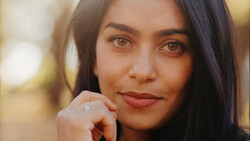 Woman with long dark hair resting her chin on her hand, gazing directly at camera with warm expression.