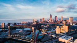 Cleveland skyline at golden hour with industrial waterfront featuring red cargo cranes and shipping containers.