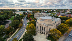 Aerial view of a domed classical building surrounded by trees and urban landscape with river.