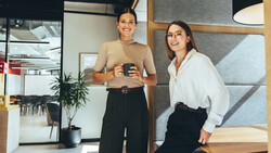 Two women smiling in a modern office space, one holding a phone.