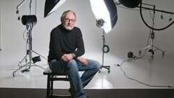 Man sitting on stool in professional studio with softbox lighting setup.