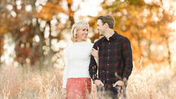 Couple walking together in an autumn field with warm, golden-hour backlighting.