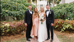 Bride and groom pose with two groomsmen in a garden courtyard surrounded by ivy and flowering shrubs.