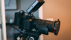 Professional cinema camera with prime lens mounted on tripod head with external monitor attached.