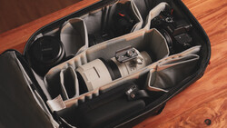 Open camera bag with organized compartments holding a telephoto lens, camera body, and accessories on a wooden surface.