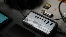 Multi-port USB hub with card reader and cables on dark desk surface.
