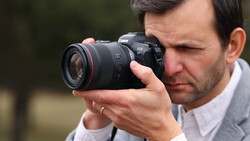 Photographer holding Canon EOS R5 mirrorless camera with RF lens to eye while composing shot.