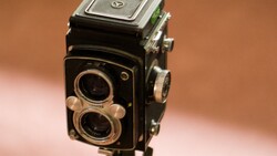 Vintage twin-lens reflex camera with chrome accents and dark body against warm brown background.