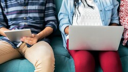 Three people sitting on a teal couch, each holding a laptop or tablet device.